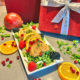 Weihnachtlich angerichtetes Orange-Glazed Chicken auf Salatbett mit Beeren, Orangenscheiben und Granatapfelkernen vor roter Geschenkdeko.